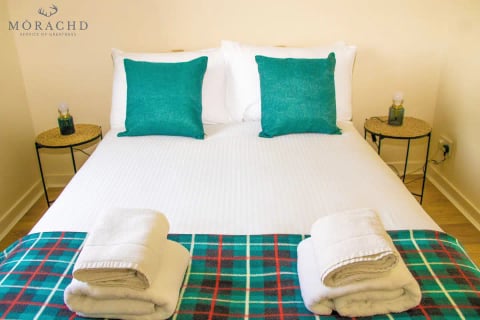 King bed with teal cushions and tartan runner