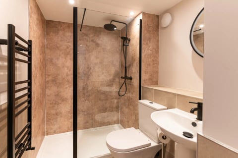 Shower room with copper-toned stone panelling and black fittings