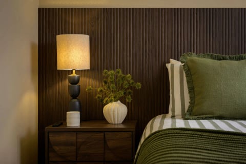 Bedside styling with sculptural lamp against dark timber slats