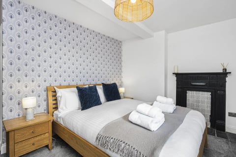 Oak bed with navy cushions and leaf-print wallpaper