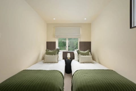 Twin beds with green throws beneath the window