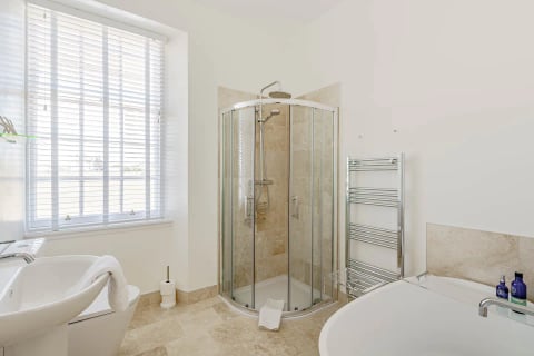 Corner shower with heated towel rail in travertine bathroom