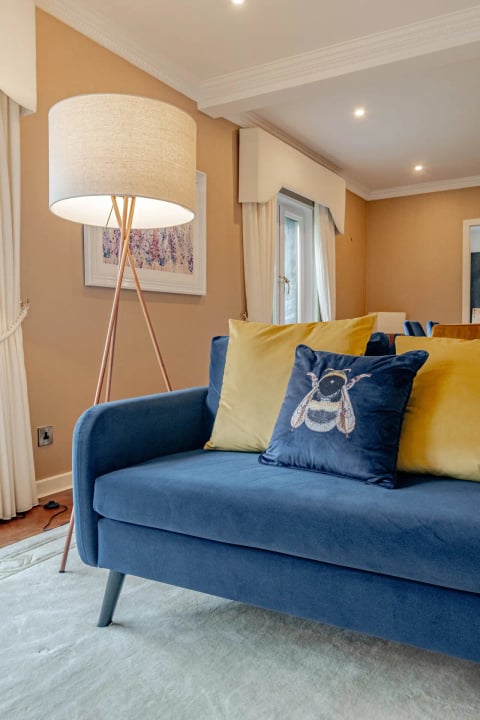 Navy sofa with bee and mustard cushions under a tripod lamp