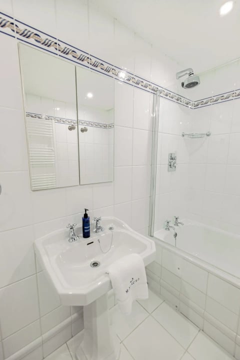 White bathroom with over-bath shower and pedestal basin