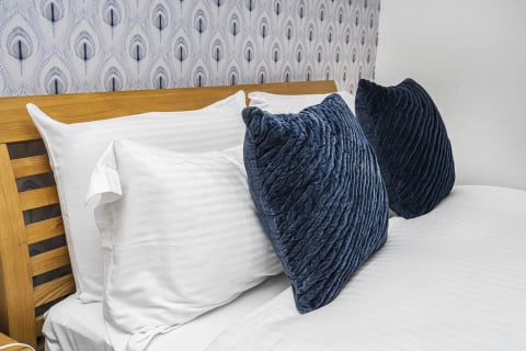 Peacock wallpaper behind the oak bed with navy cushions