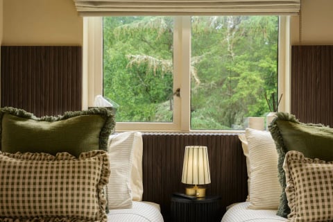 Twin beds by the window with lamp between, woodland outside