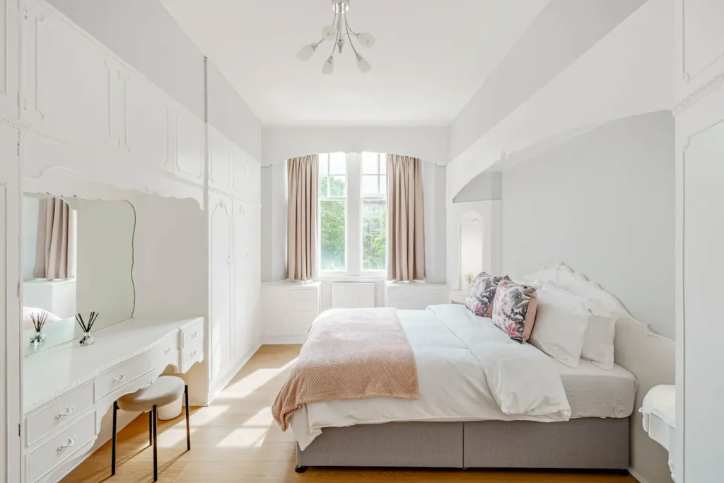 Minimalist bedroom with a cozy bed, large windows, white vanity, and soft natural light.