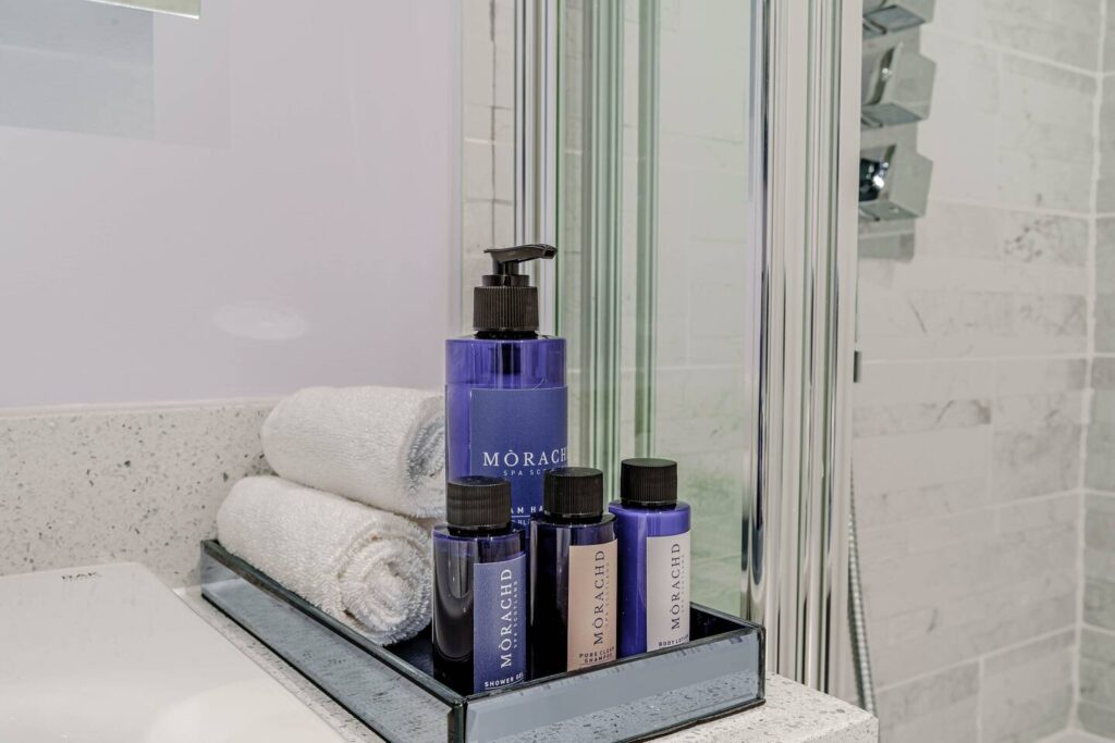 Luxury bathroom toiletries and towels on a tray beside a glass shower in a modern bathroom setting.