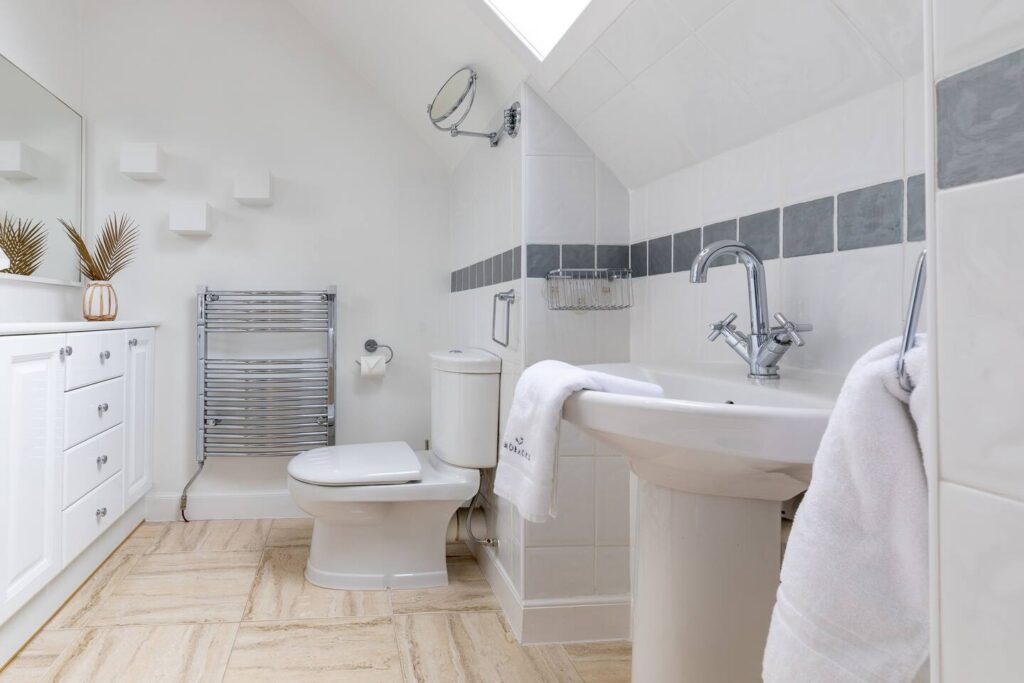 Modern white bathroom with chrome fixtures, towel rack, sink, and toilet, showcasing a minimalist decor style.