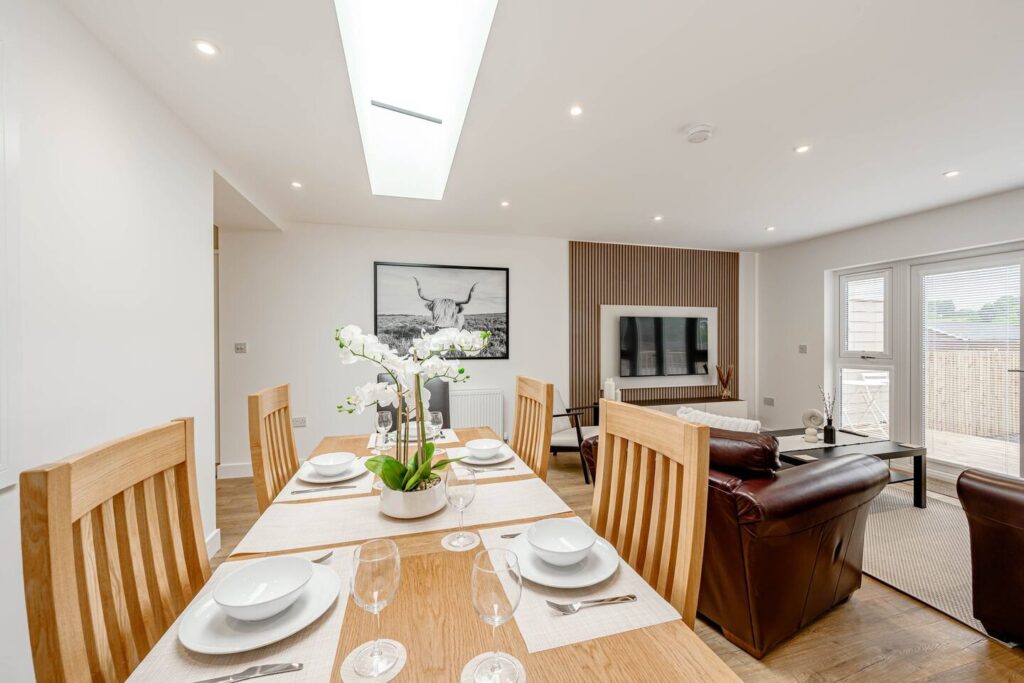 Modern open-plan dining and living area with wooden table, leather sofas, and large window for natural light.