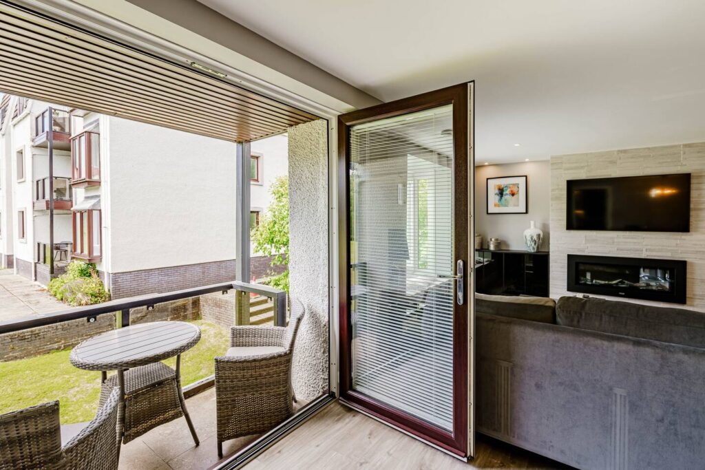 Modern living room with open balcony door, rattan furniture, and TV, showcasing cozy and stylish home interior.