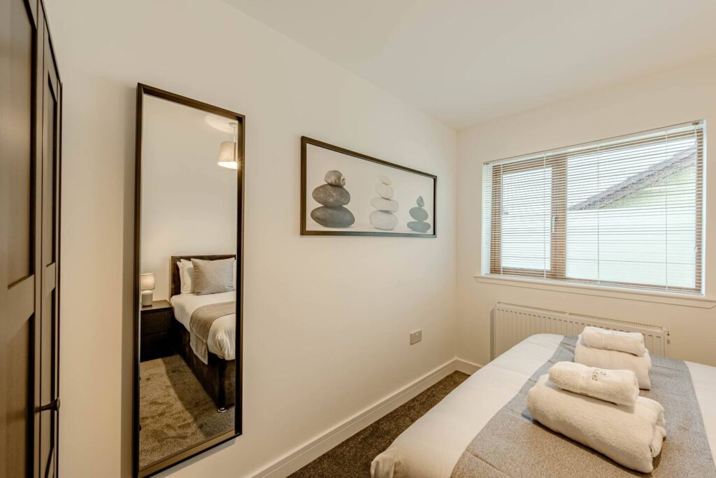 Modern bedroom with minimal decor, large mirror, and soft lighting. Clean and inviting space with folded towels on bed.