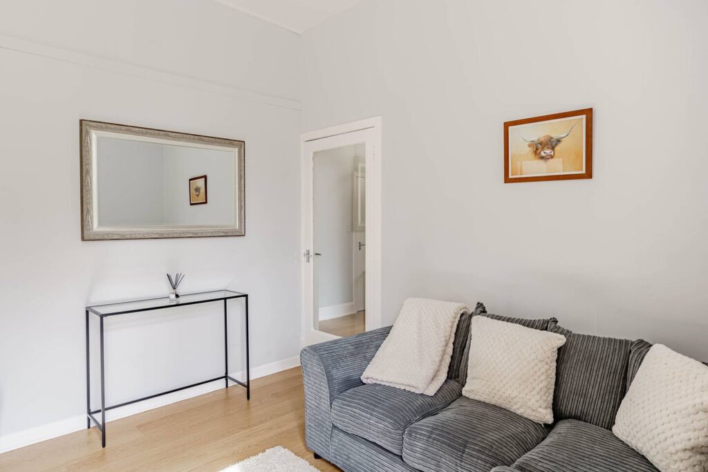 Modern living room with grey sofa, wall mirror, and minimalist decor. Light wood flooring and bright, inviting atmosphere.