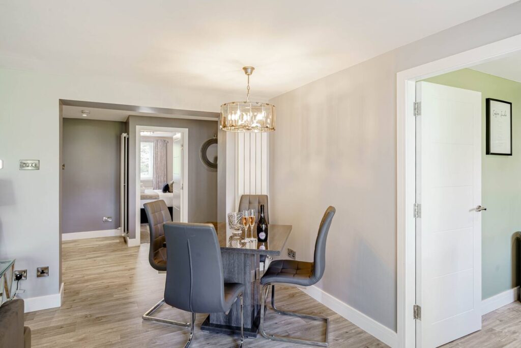 Modern dining area with a glass table, gray chairs, and elegant lighting in a cozy, open-plan home interior.