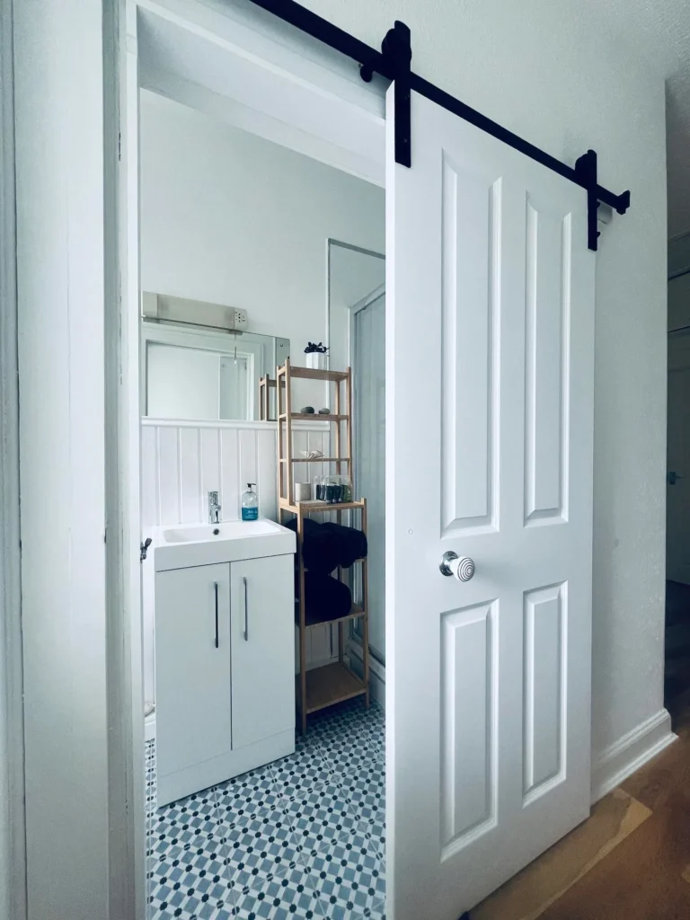 Modern bathroom with sliding door, white sink cabinet, and geometric tile floor.