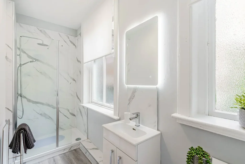 Modern bathroom with glass shower, white vanity, and illuminated mirror.