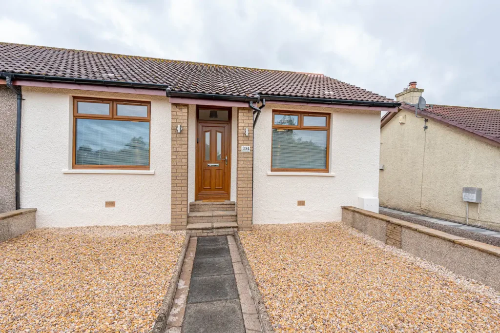 Cozy single-story house with a pebbled front yard, brown roof, and welcoming wooden door.