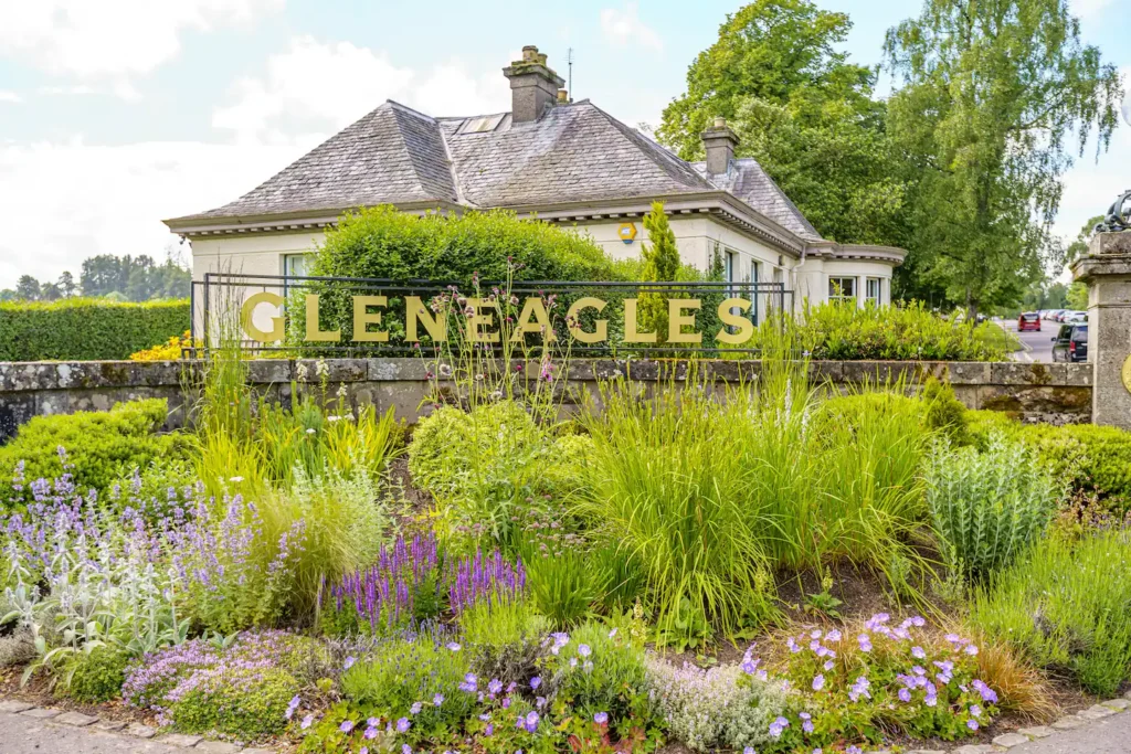 Entrance to Gleneagles Hotel surrounded by lush gardens and vibrant purple flowers on a sunny day.