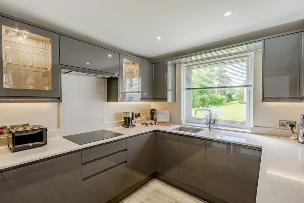 Modern kitchen with sleek gray cabinets, large window view, and built-in appliances on a white countertop.