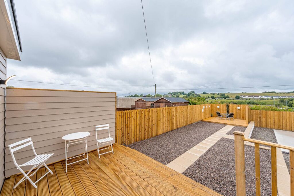 Spacious wooden deck with white patio set overlooking fenced backyard and landscape on a cloudy day.