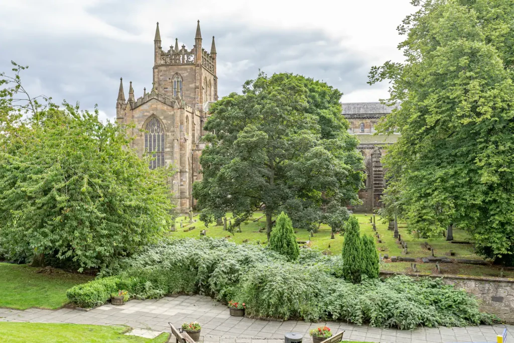 Historic stone church surrounded by lush greenery and trees in a peaceful cemetery setting.