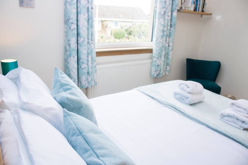 Cozy bedroom with blue decor, neatly arranged pillows, towels, and a view through the window.