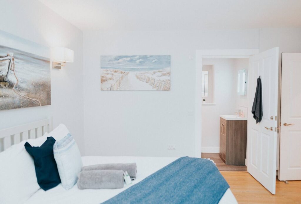 Cozy bedroom with beach-themed decor, blue pillows, and en-suite bathroom for a relaxing retreat.