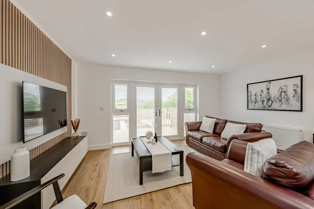 Modern living room with leather sofas, large TV, and natural light from glass doors. Cozy and stylish interior design.