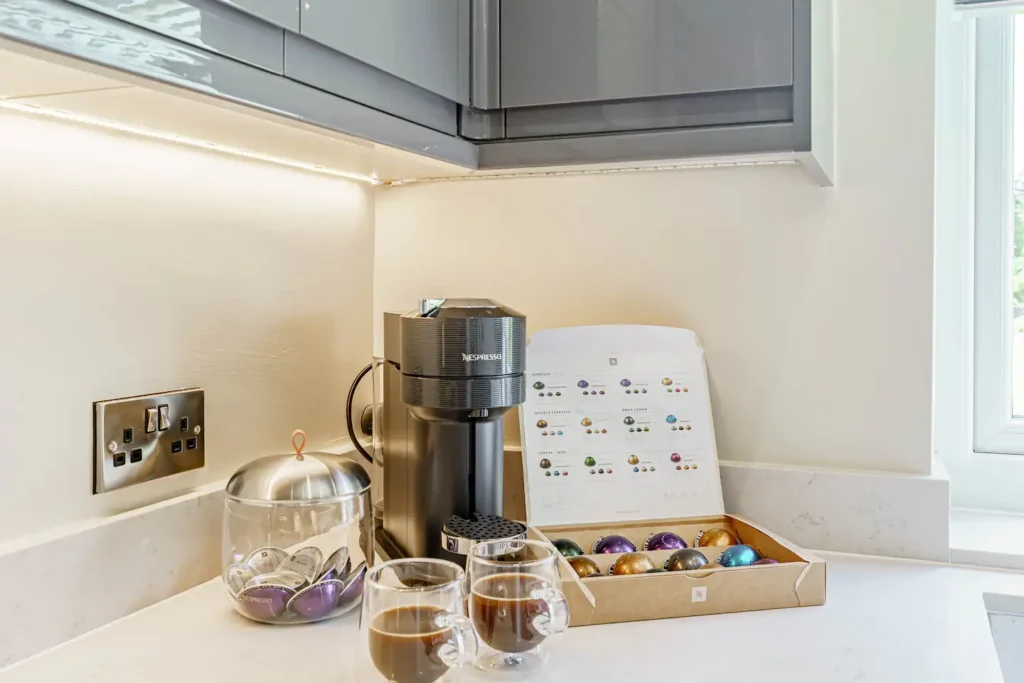 Modern kitchen corner with Nespresso machine, colorful coffee pods, and two mugs of coffee on a white countertop.