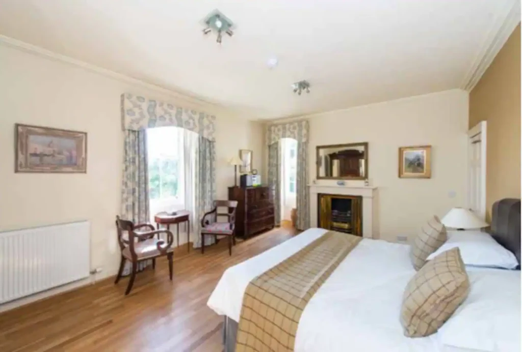 Elegant bedroom with classic decor, double bed, wooden furniture, and large windows overlooking a garden.