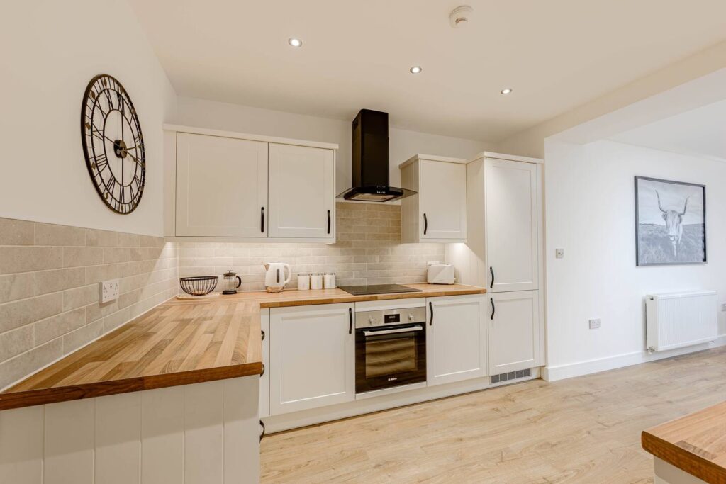 Modern kitchen with white cabinets, wood countertops, and stainless steel appliances. Wall clock and art decor.