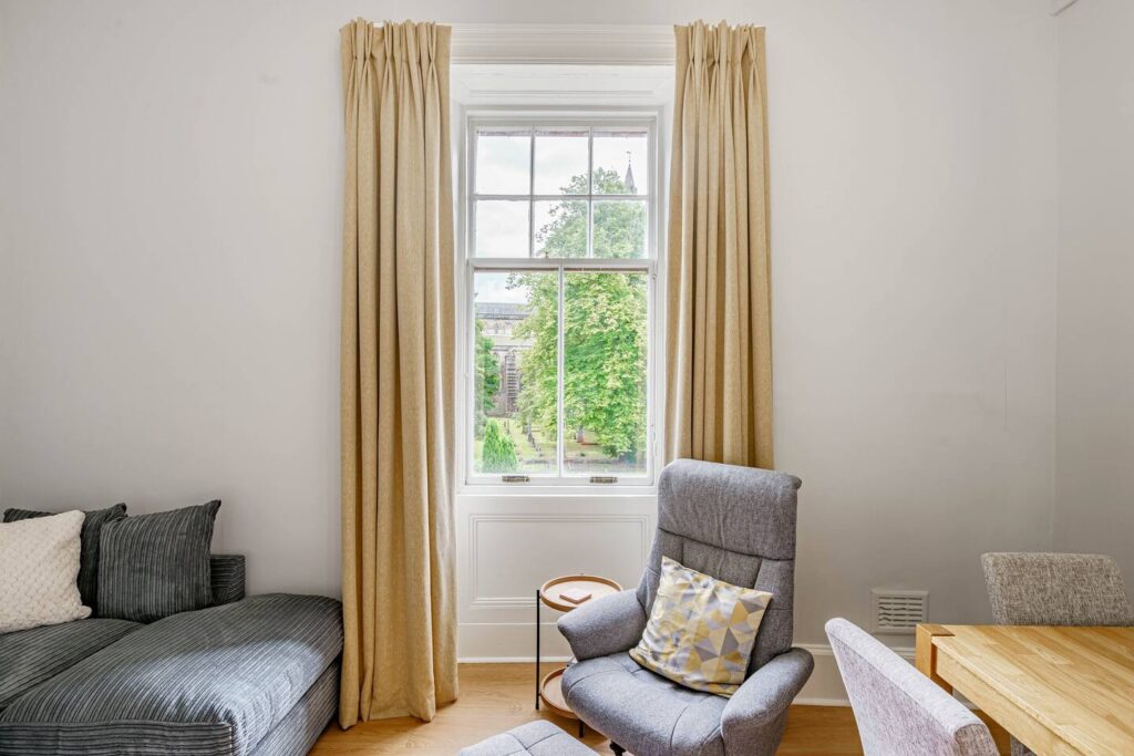 Bright living room with comfy chair, sofa, and window view of lush trees. Cozy home interior design.