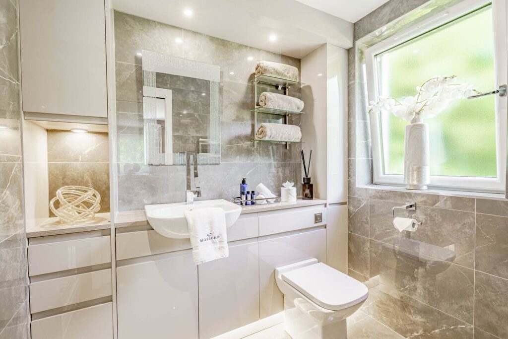 Modern bathroom with marble tiles, sleek vanity, and elegant decor near a frosted window.