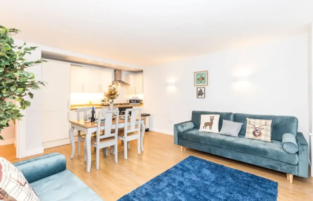 Modern living room with blue sofa, dining area, kitchen, and cozy decor. Bright and inviting open-plan space.