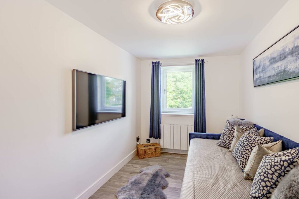 Modern cozy living room with wall-mounted TV, daybed, and decorative pillows. Bright window view enhances the space.