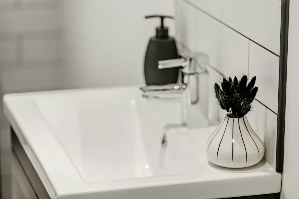 Modern bathroom sink with a black soap dispenser and decorative vase on a white countertop.