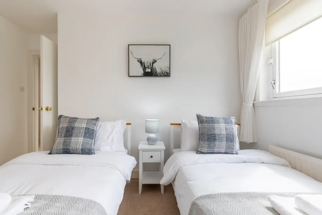 Minimalist twin bedroom with white bedding, grey pillows, and framed art on the wall, creating a cozy, serene atmosphere.