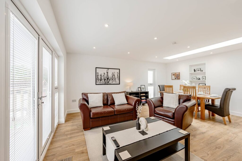 Modern living and dining area with leather sofas, wooden floor, and elegant decor in a well-lit room.