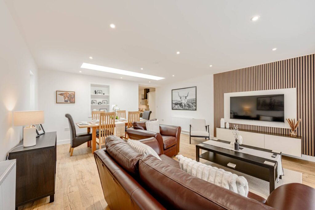 Modern living room with leather sofas, dining table, wall-mounted TV, and stylish decor elements.