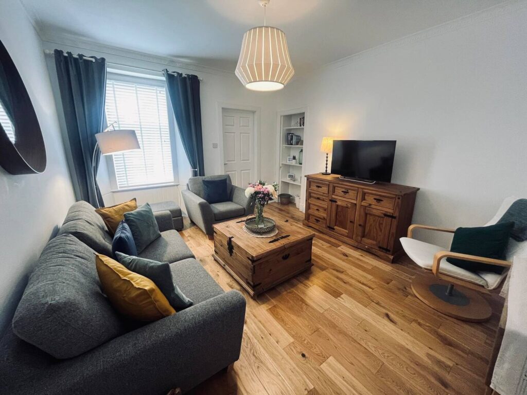 Cozy living room with grey sofas, wooden furniture, and modern decor in soft natural lighting.