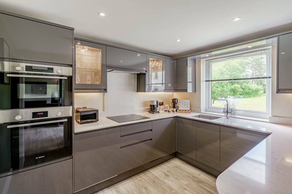 Modern kitchen with sleek grey cabinets, built-in ovens, and large window offering a scenic view.