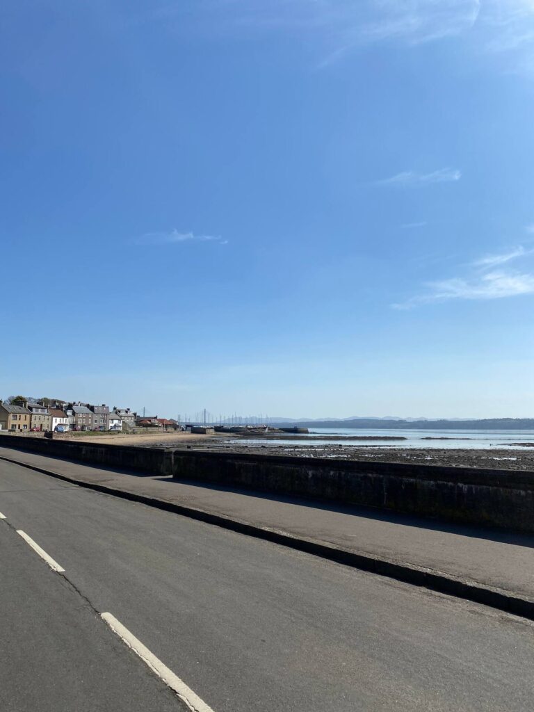 Coastal road with clear blue sky, houses, and marina in the background, perfect for travel content.