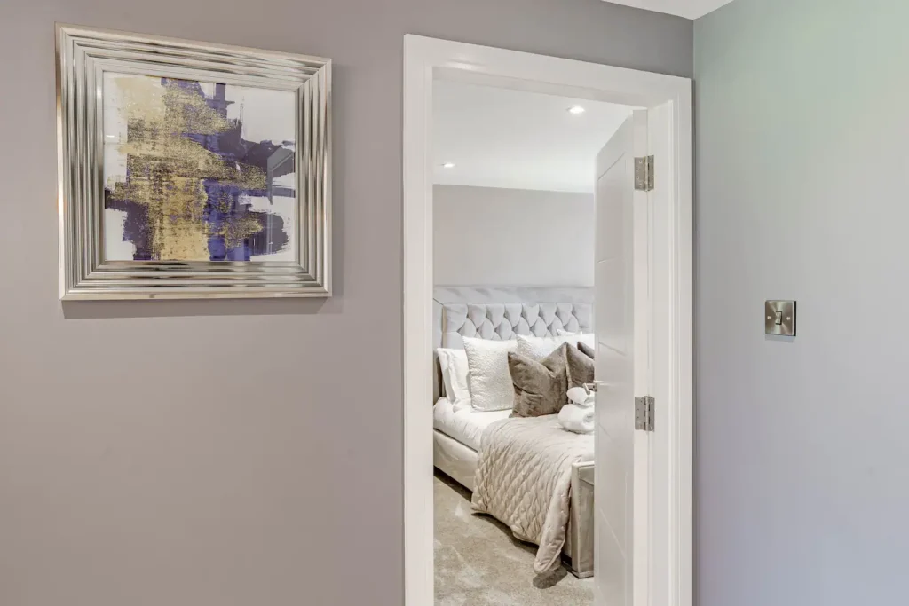 Modern bedroom view through open door, art on wall, plush décor, neutral tones.