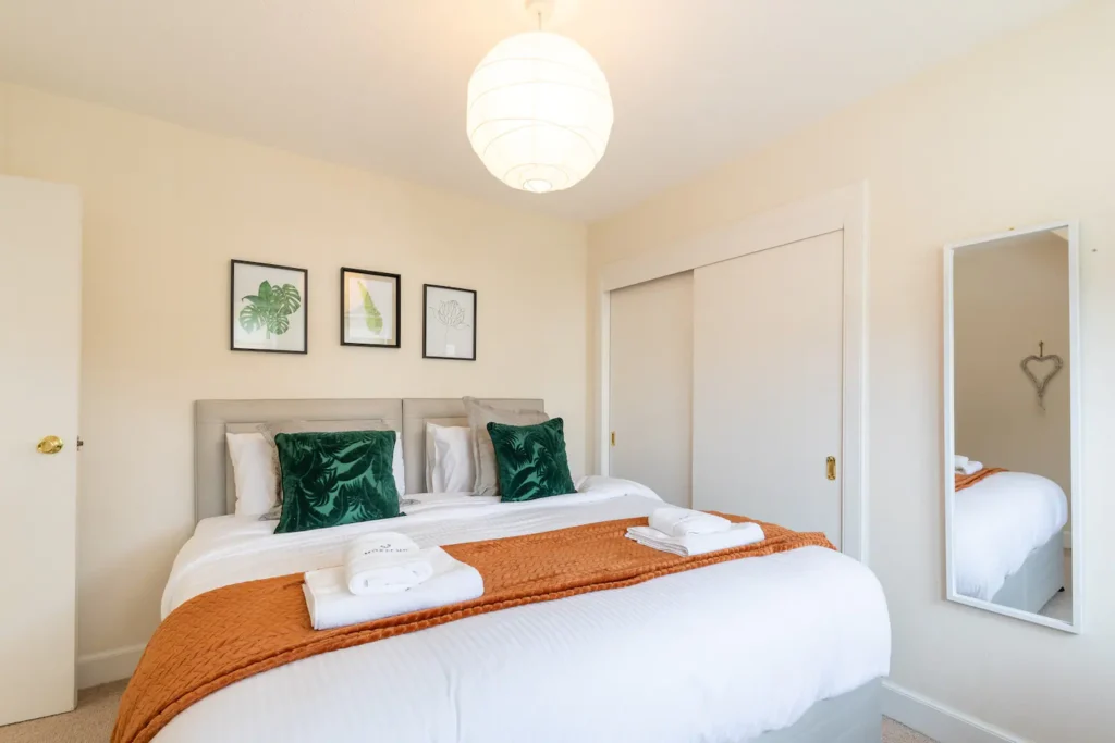 Cozy bedroom with a king-sized bed, green pillows, and wall art, featuring warm lighting and minimalist decor.