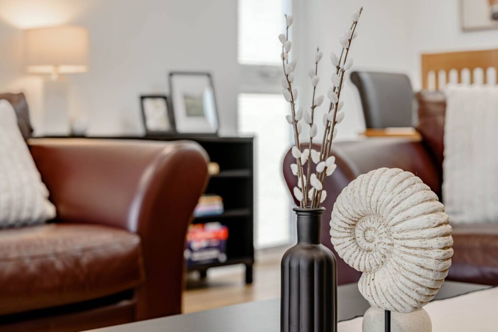 Modern living room with leather sofa, decorative vase, and spiral shell sculpture on table. Cozy interior design.