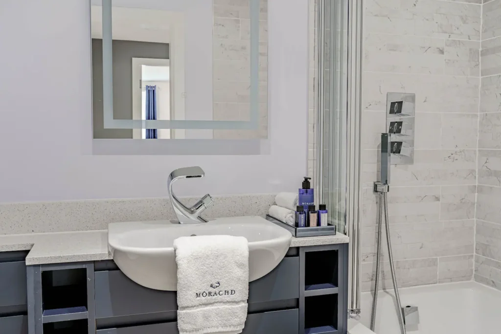 Modern bathroom with stylish sink, marble tiles, and luxury toiletries on a countertop with a mirror reflection.