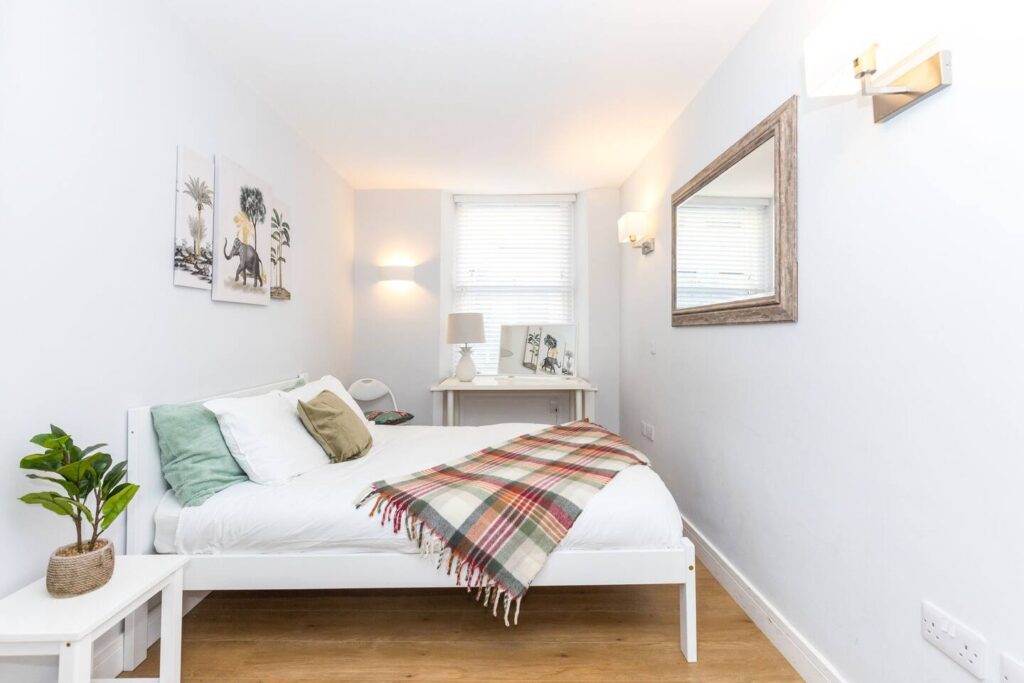 Bright, cozy bedroom with a modern white bed, plaid throw, and wall art, featuring a mirror and natural light.