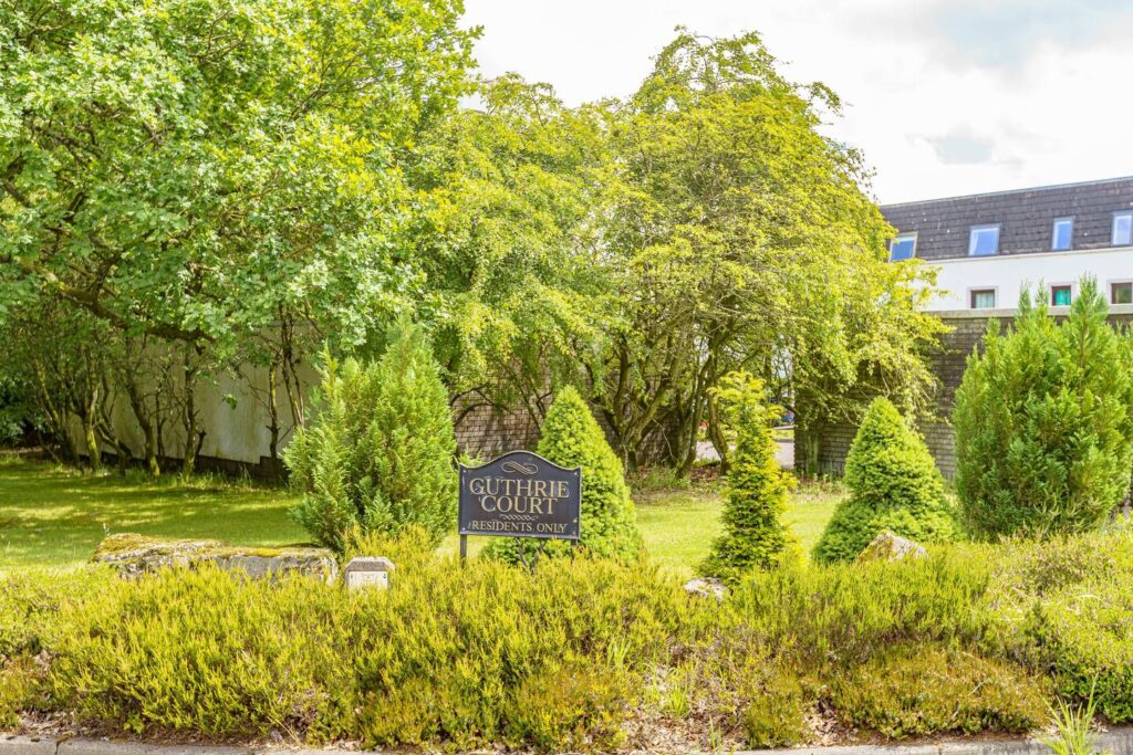 Guthrie Court entrance sign surrounded by lush greenery and trees, highlighting a peaceful residential area.