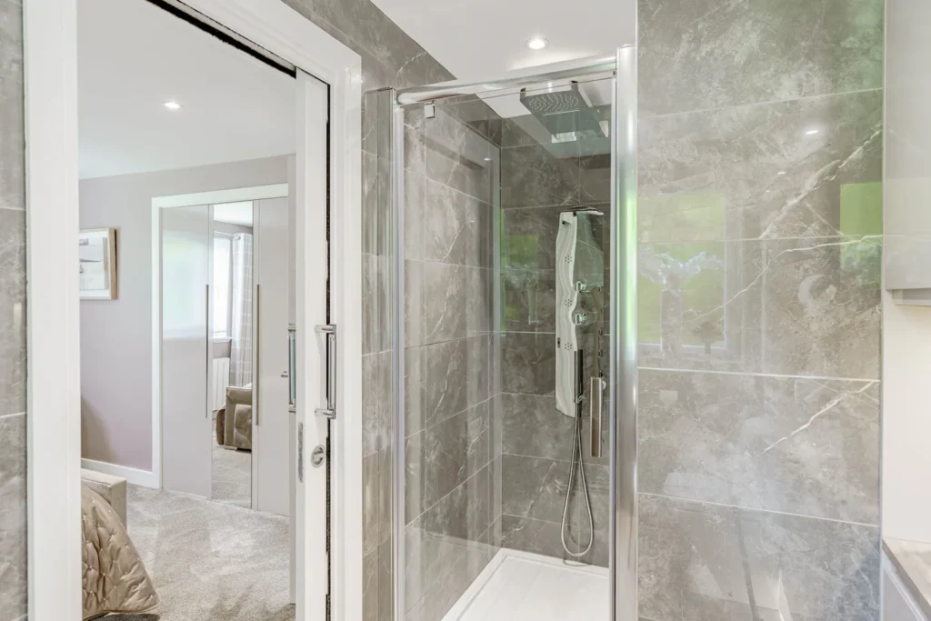 Modern bathroom with sleek glass shower and gray marble tiles, reflecting a cozy adjacent room with carpet.