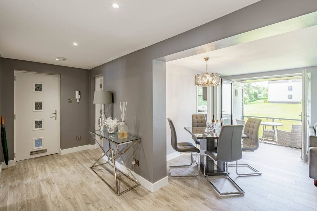 Modern open-plan dining area with stylish decor, wooden flooring, and a glass table set near a garden view.